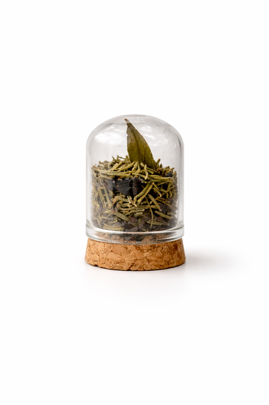 Glass container with cork base holding dried green tea leaves on a white background
